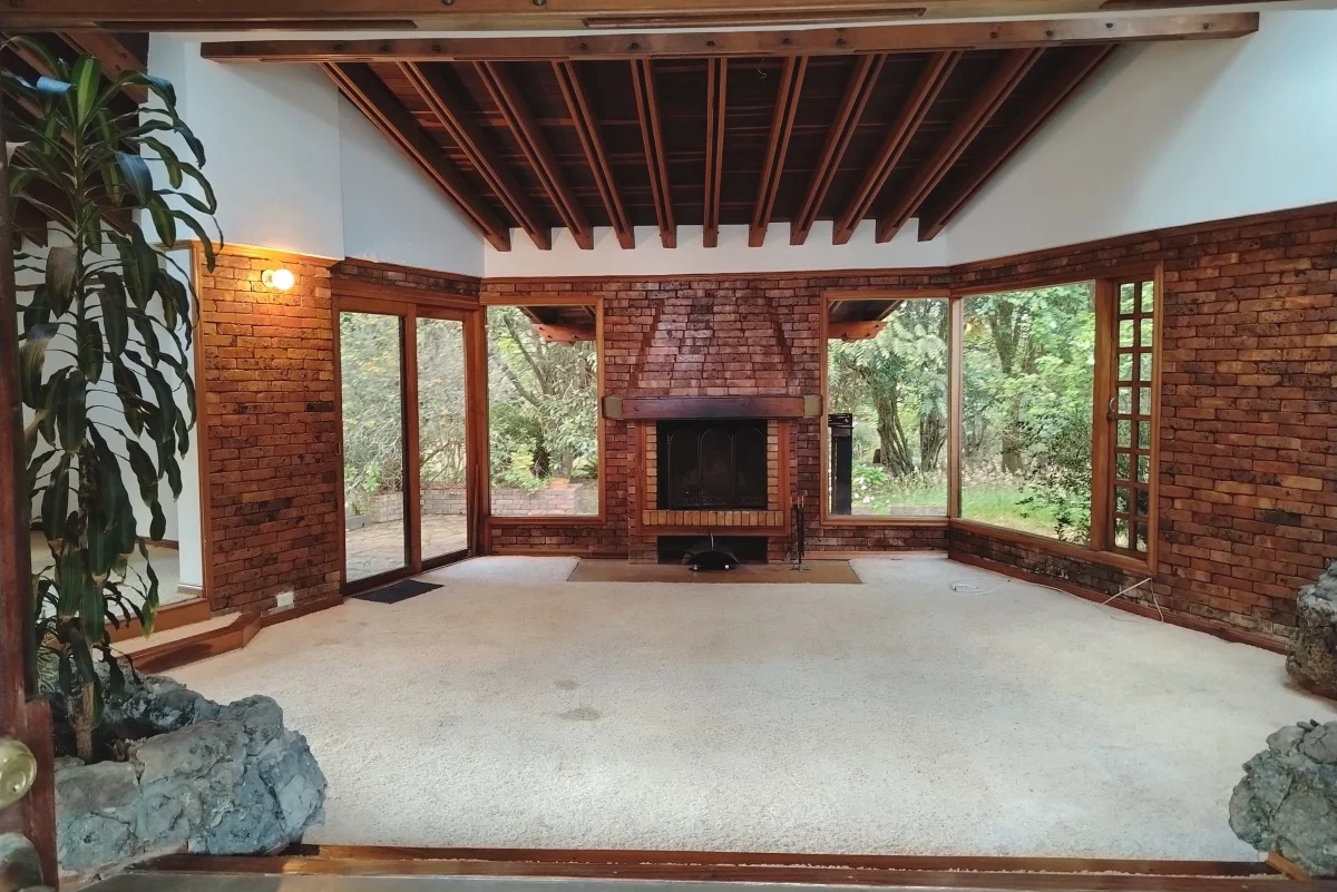 Sala principal con chimenea, vigas de madera y grandes ventanales al jardín